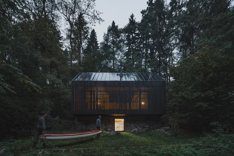 Slatted timber facade glowing with interior light at dusk beside a beached boat