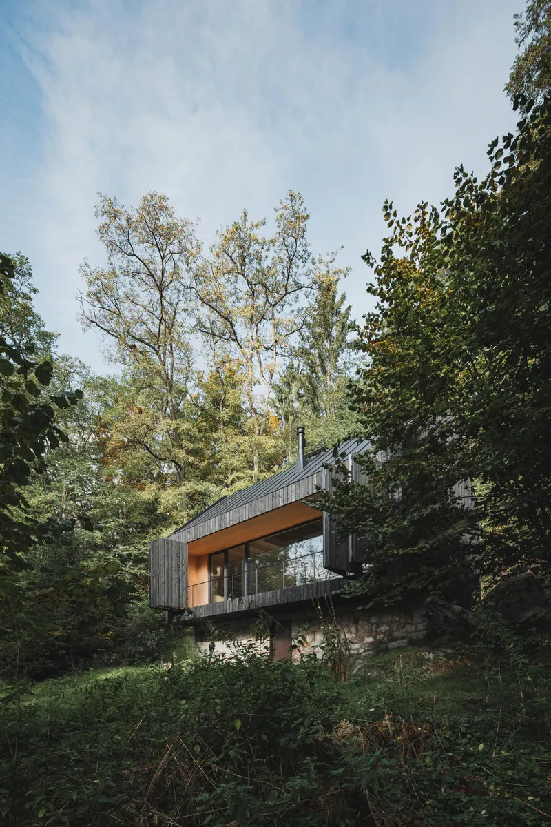 Elevated timber volume on stone base nestled among deciduous trees in dappled daylight
