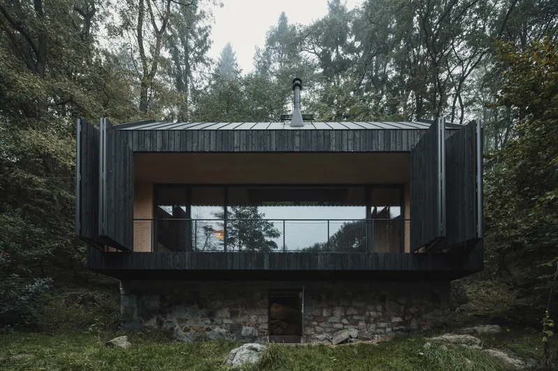 Charred wood facade with central glass opening spanning stone plinth foundation under overcast sky