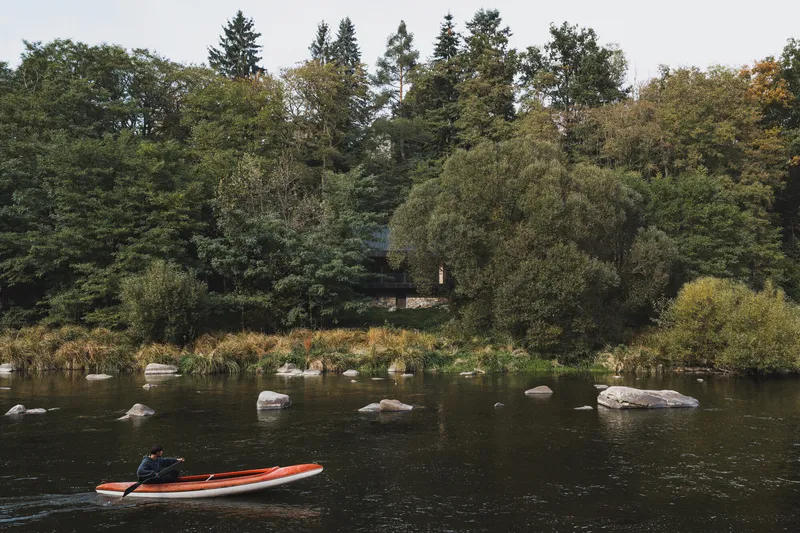 Distant view from the river showing the structure nestled among dense trees with a kayak