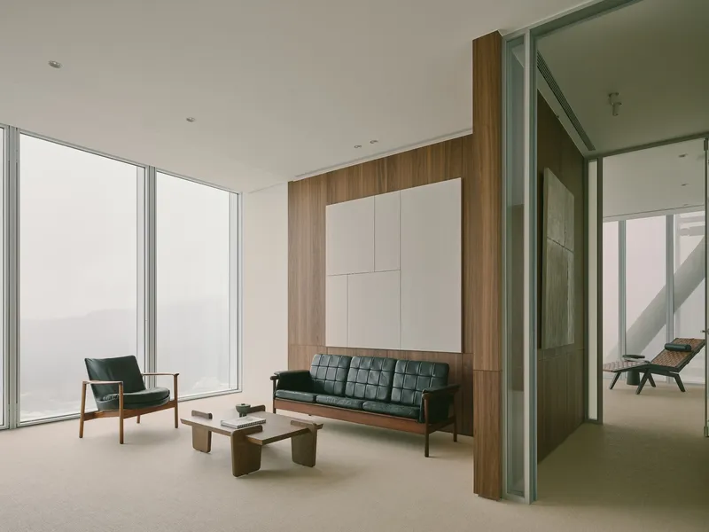 Seating area with walnut wall panel, white ceiling-mounted storage, and glazed partition to adjacent room