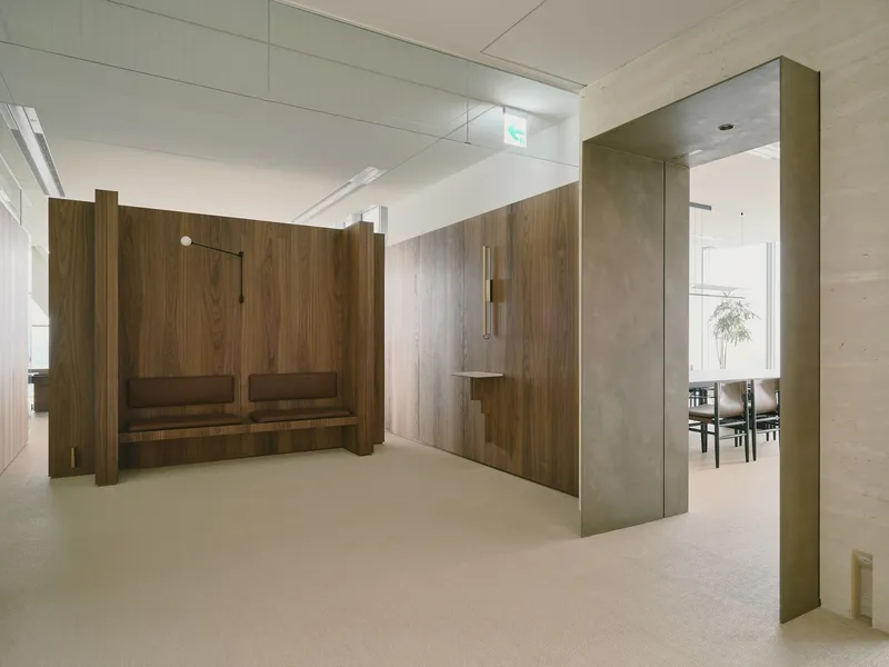 Walnut partition walls with built-in bench seating and brass-clad columns framing the circulation space