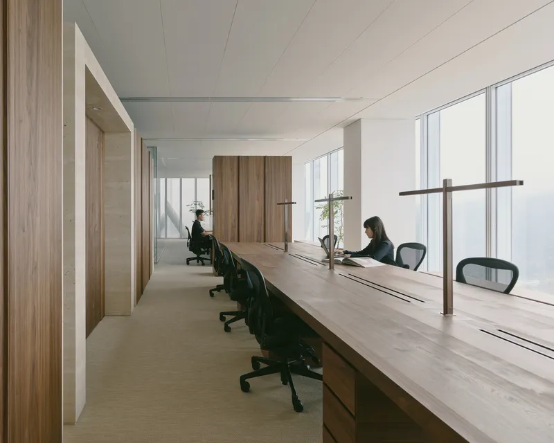 Shared workspace along the window wall with two occupants at timber desks in natural daylight