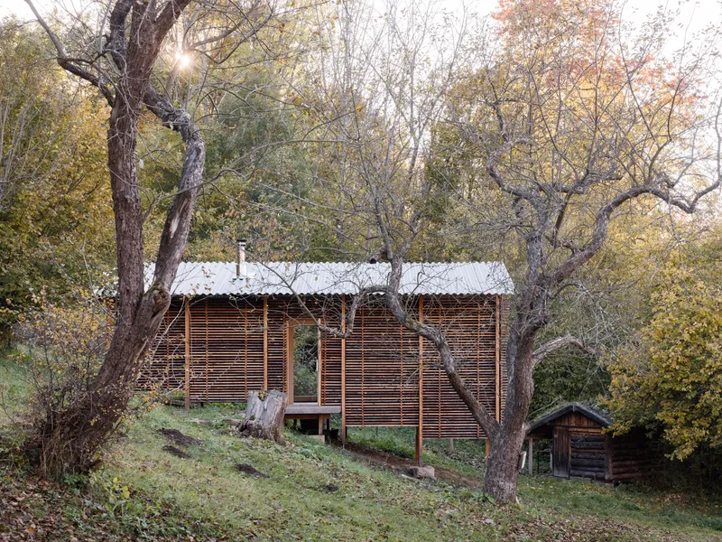 Gabled cabin with horizontal timber slat screens nestled among deciduous trees in autumn foliage
