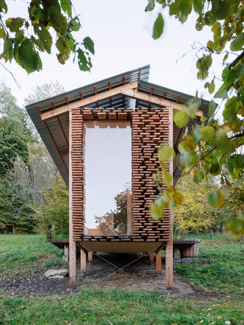 Front facade showing vertical timber louvers and large glazed opening framed by overhanging birch branches