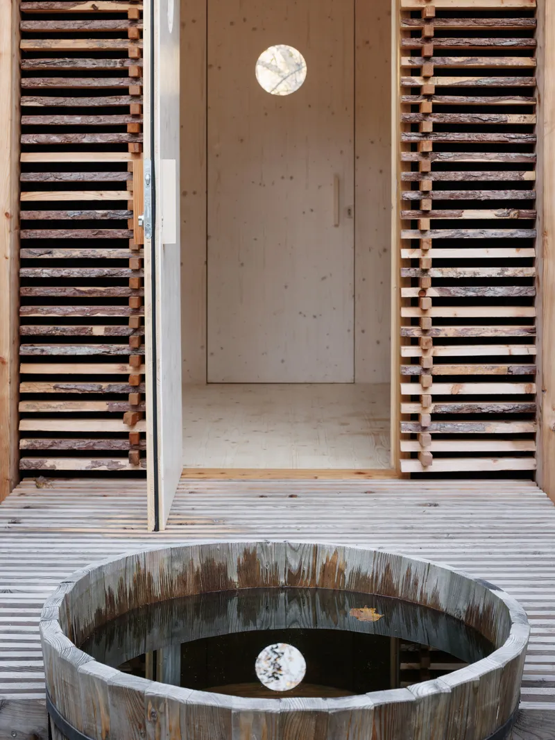 View through open doorway showing circular window reflected in water filled wooden barrel on slatted deck