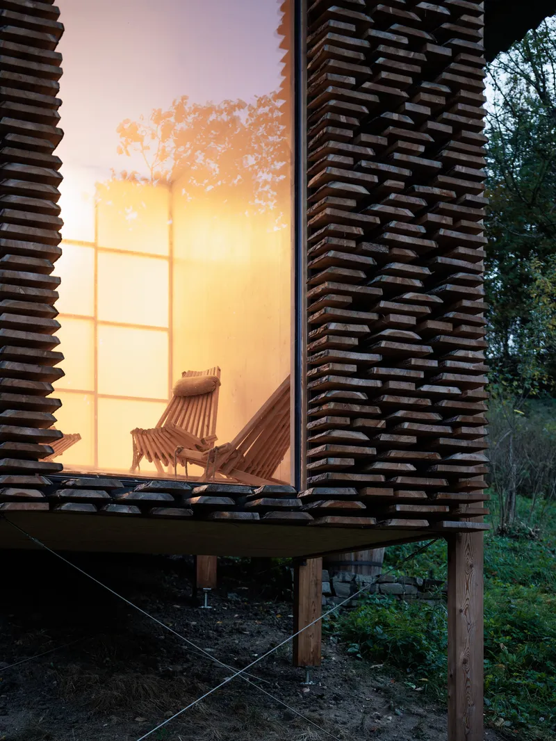 Stacked timber slat facade with corner window glowing at dusk, elevated on timber posts