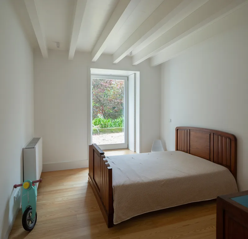 Bedroom with timber bed frame and glass door opening to planted courtyard in daylight