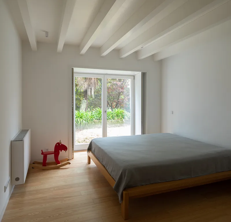 Bedroom with timber platform bed and double glass doors framing view of garden vegetation