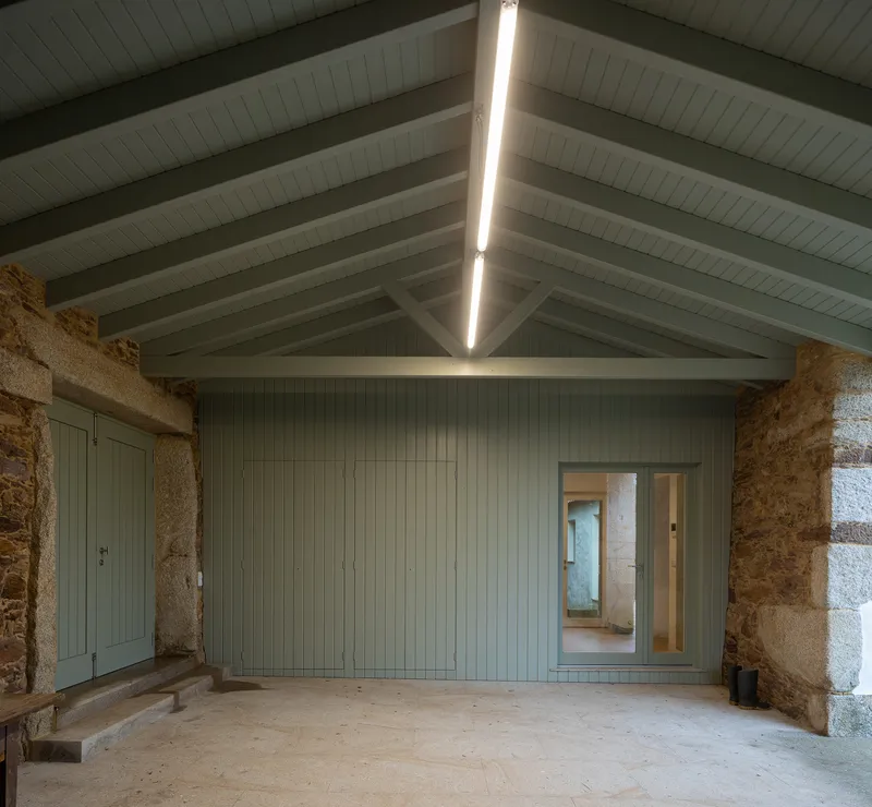 Interior with exposed timber rafters, skylight slot, and vertical paneled wall between granite stone corners