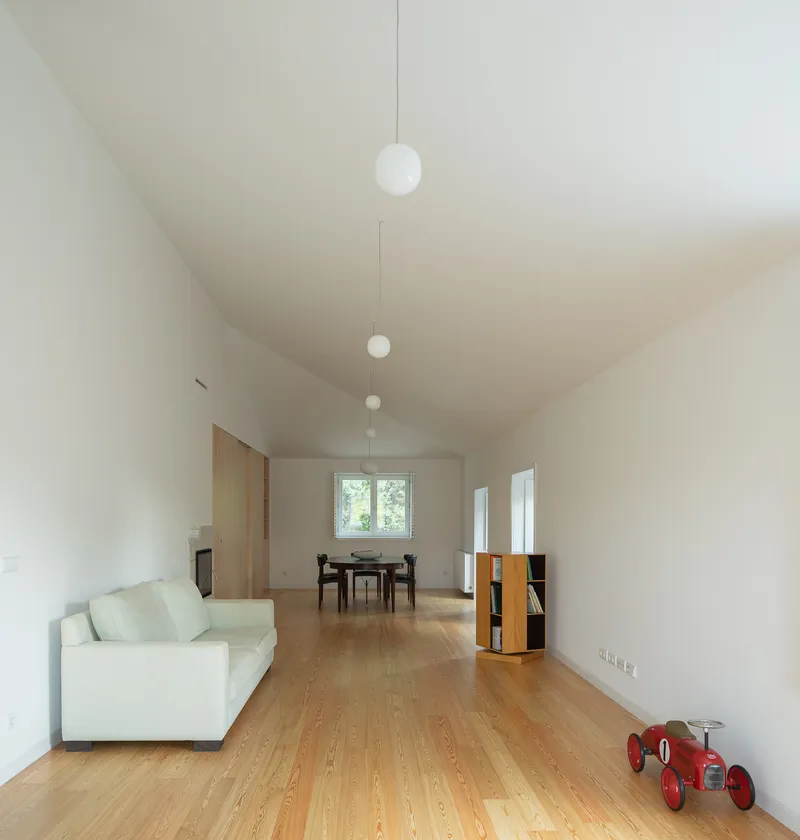 Open living space with oak flooring, vaulted ceiling and pendant lights suspended in a row