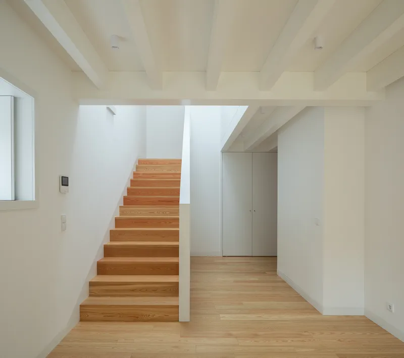 Timber staircase with exposed ceiling beams rising through a double-height volume with wood flooring