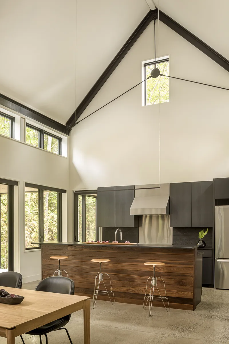 Kitchen island with walnut face and steel stools beneath exposed timber roof structure