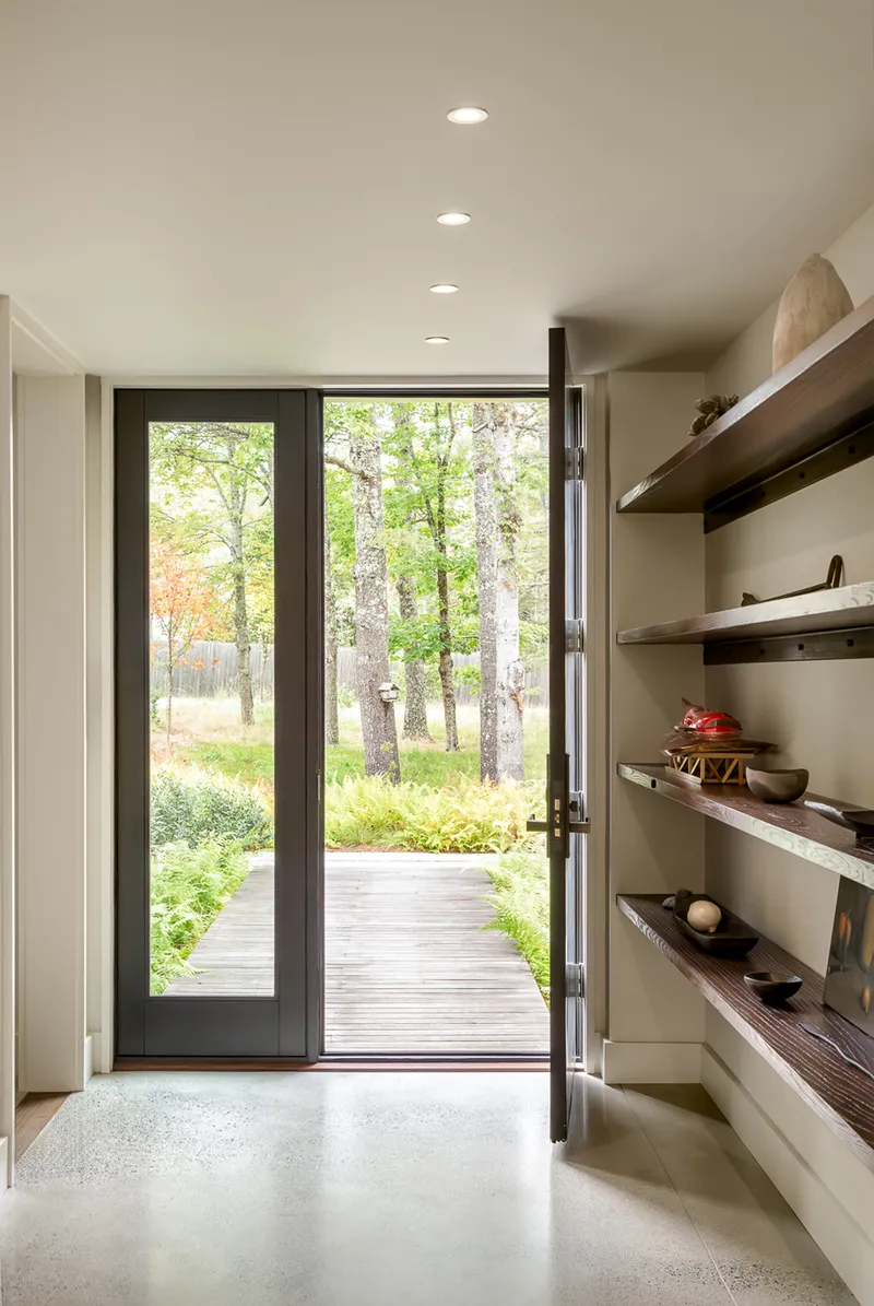 Entry hall with glazed door opening to a timber boardwalk through the forest and timber shelving along one wall
