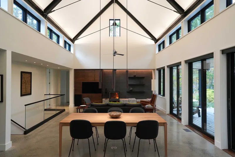 Living space with exposed timber trusses, clerestory windows, fireplace, and polished concrete floor below vaulted ceiling