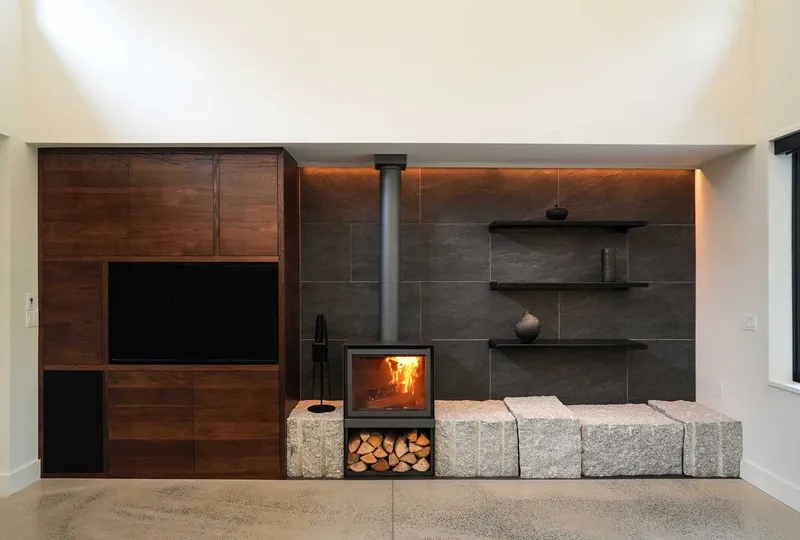 Living room wall featuring walnut cabinetry, a woodstove with firewood storage, and rough granite block bench