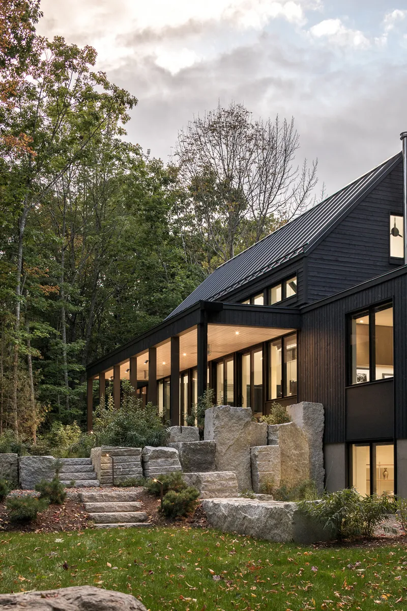 Black-stained wood facade with clerestory windows, terraced stone steps, and boulders under cloudy sky