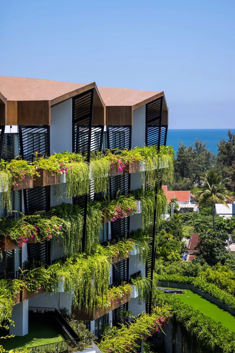 Corner elevation showing zigzag balconies with timber cladding and planted boxes with ocean in the distance
