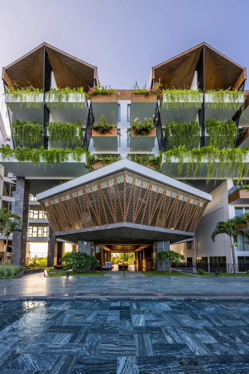 Entrance canopy with woven bamboo ceiling pattern above dark paving and reflecting pool at dusk