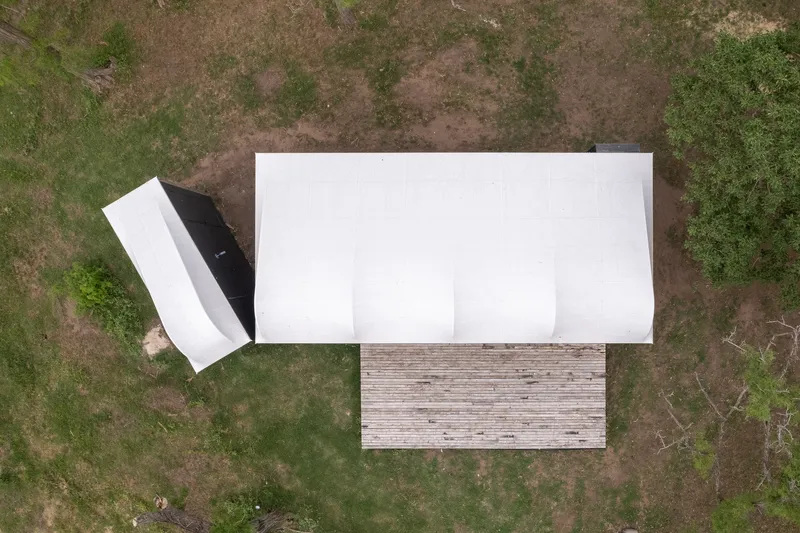 Aerial view of white barrel-vault roof and timber deck on patchy grass clearing