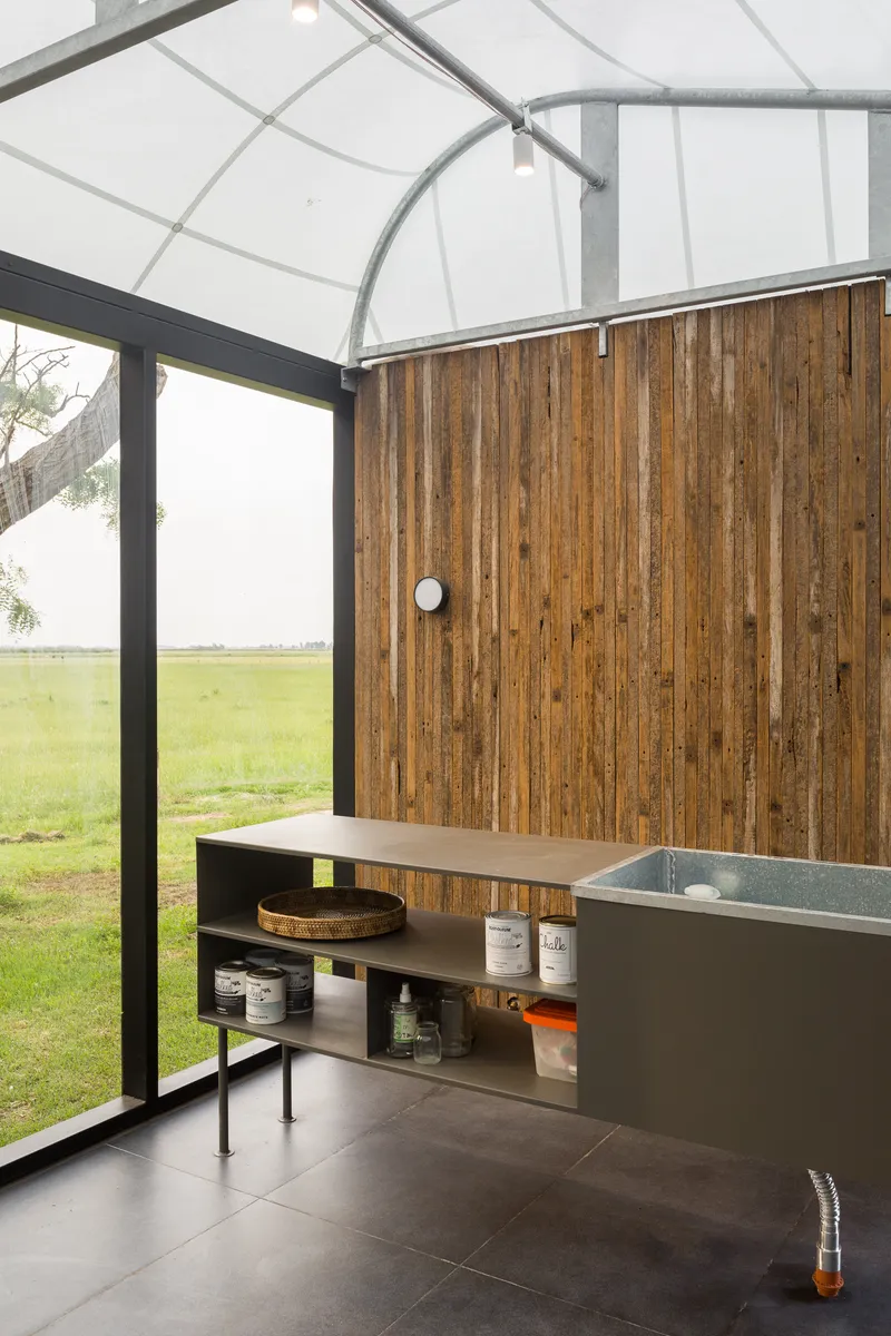 Bathroom with curved translucent roof, timber wall, terrazzo vanity, and glazed corner overlooking green field