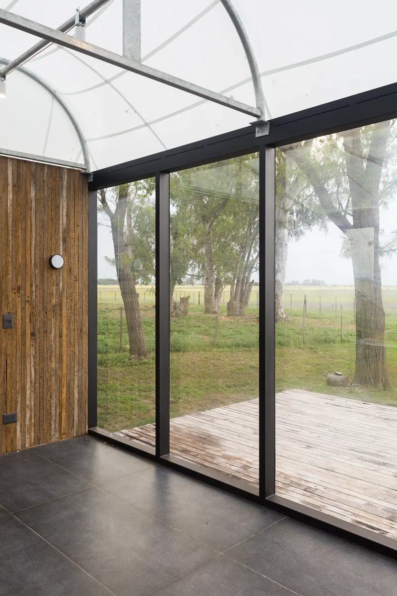 Interior view through floor-to-ceiling glazing toward timber deck and eucalyptus trees under misty grey sky