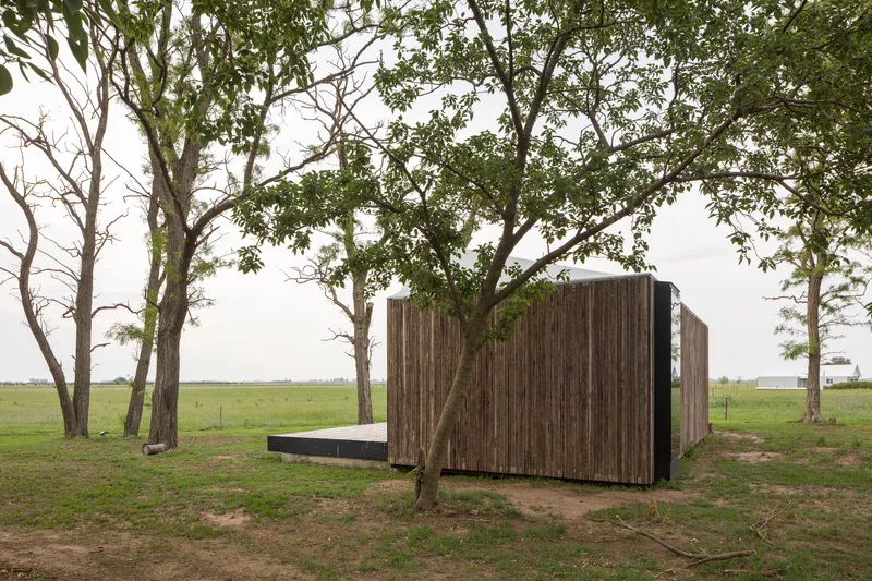Vertical timber cladding wrapping the closed volume facing open grassland with scattered trees