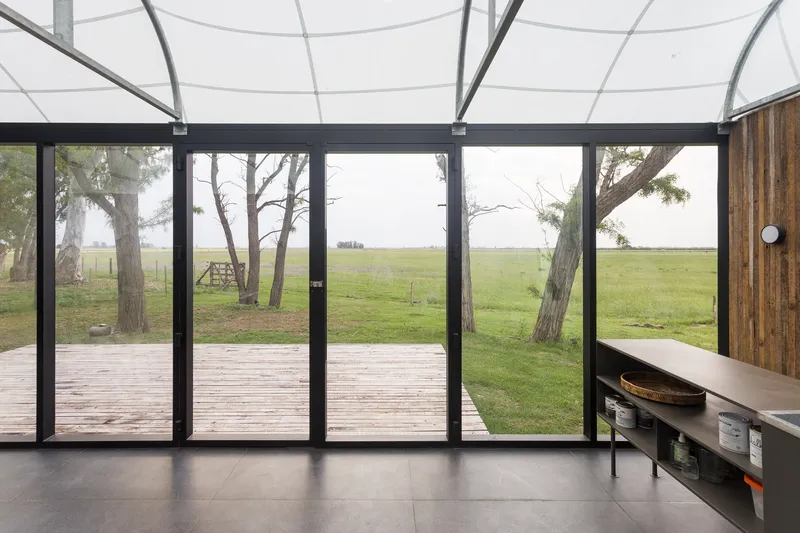 Floor-to-ceiling black-framed glass doors opening to timber deck with view of pasture and trees beyond