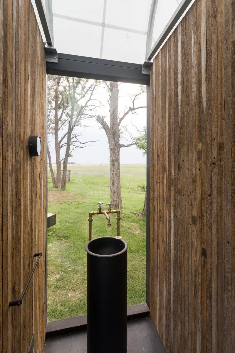 Narrow bathroom with vertical timber cladding, skylight, and cylindrical black basin facing open landscape