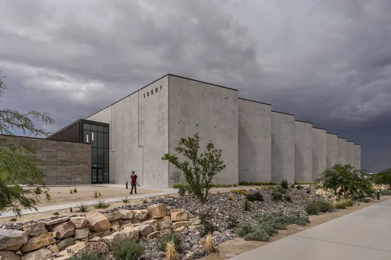 Cast concrete facade with vertical fins and desert landscaping under a dark storm sky