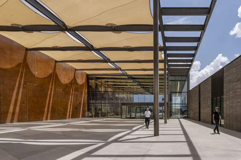 Shaded outdoor courtyard with fabric canopy and steel columns casting sharp shadows