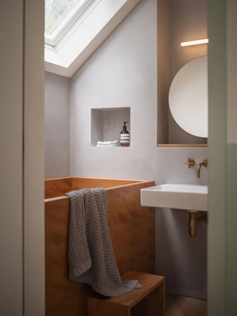 Compact bathroom with tiled tub surround and wall-mounted basin under a skylight