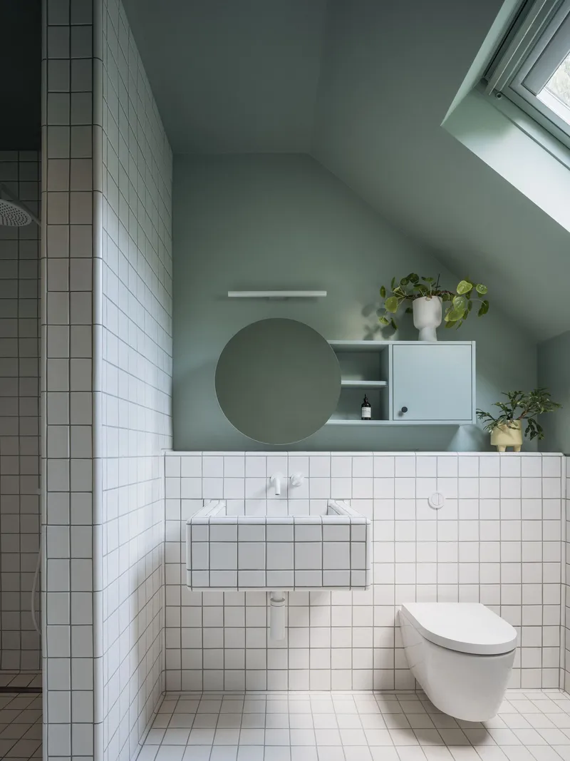 Bathroom interior showing white tiled walls, sloped ceiling with skylight, and sage green painted surfaces