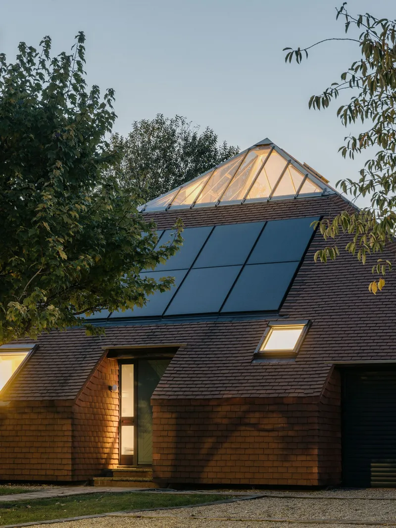 Front facade showing timber shingle cladding and rooftop solar array framed by garden trees