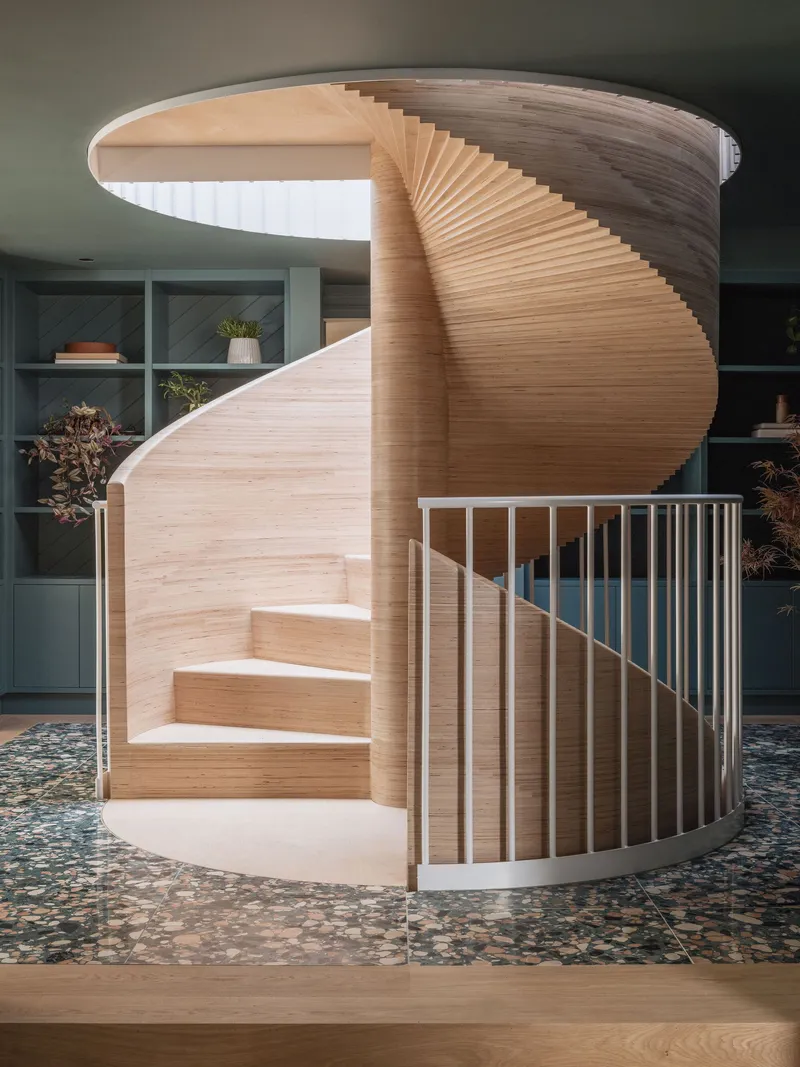 Helical timber staircase with horizontal slat detail and white metal balustrade over terrazzo flooring