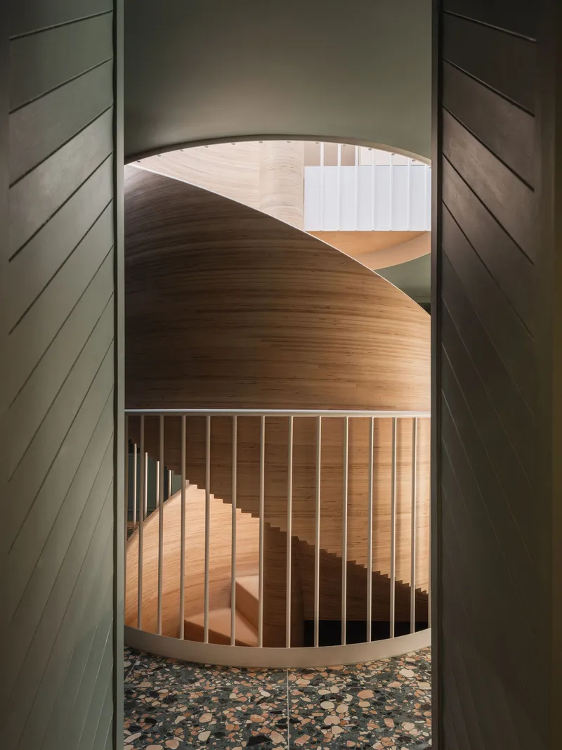 View down through the spiral stair showing layered timber treads and terrazzo floor below