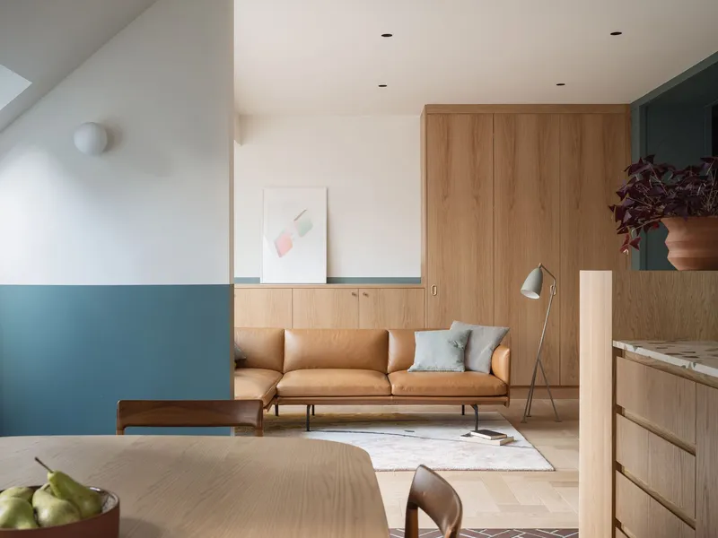 Open living area with timber cabinetry and horizontal paint band below white walls and sloped ceiling