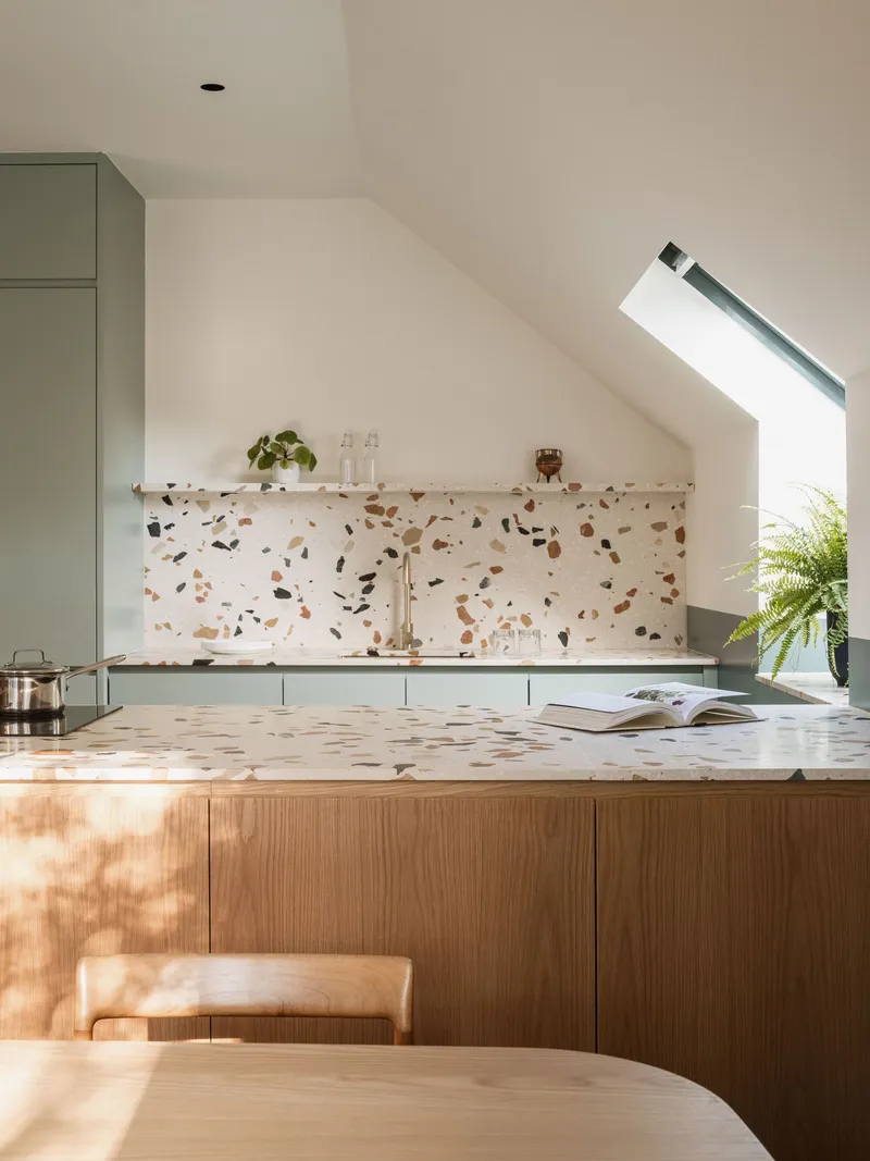 Kitchen island with terrazzo countertop and backsplash beneath an angled skylight in morning light