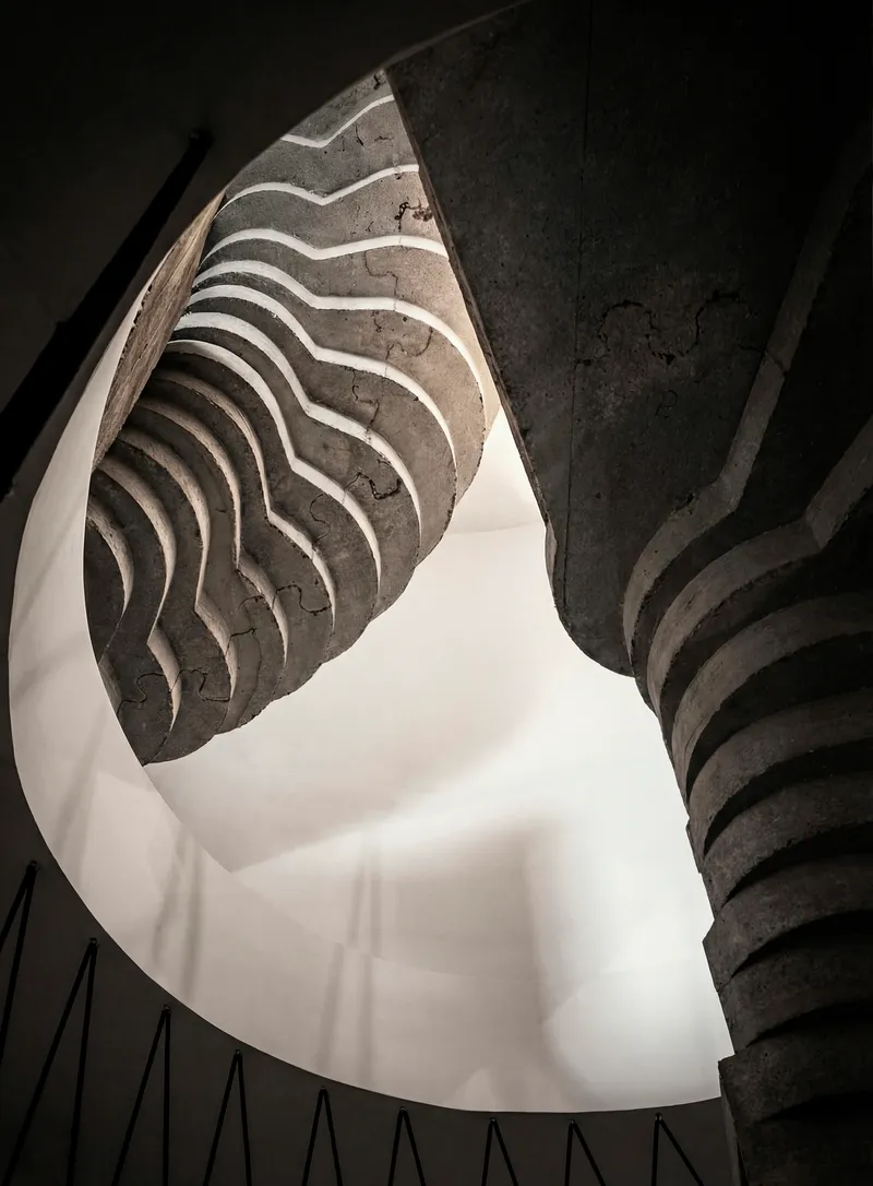 Looking up at the spiraling concrete staircase with wavy formwork patterns under natural light