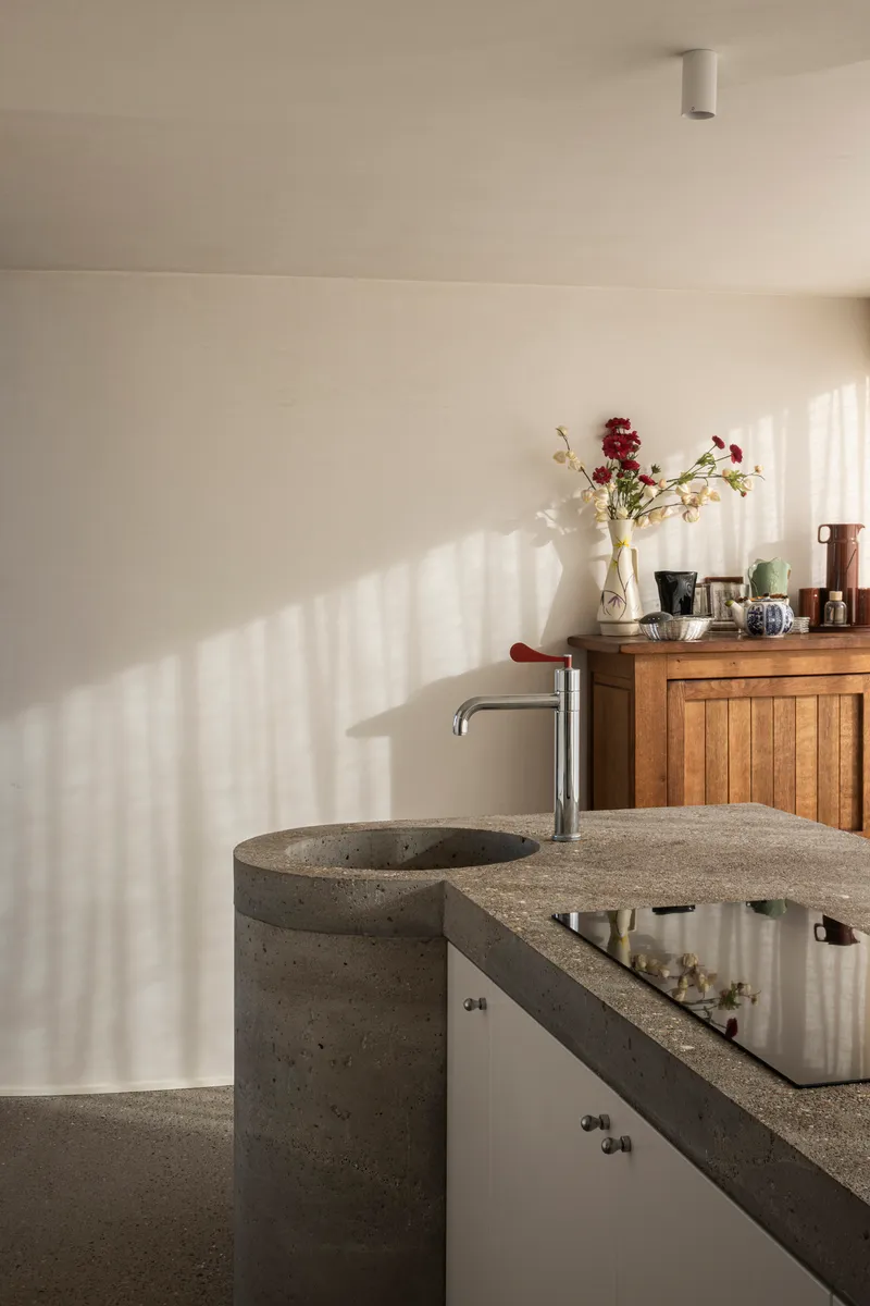 Bathroom vanity with terrazzo counter and cylindrical sink catching striped window shadows