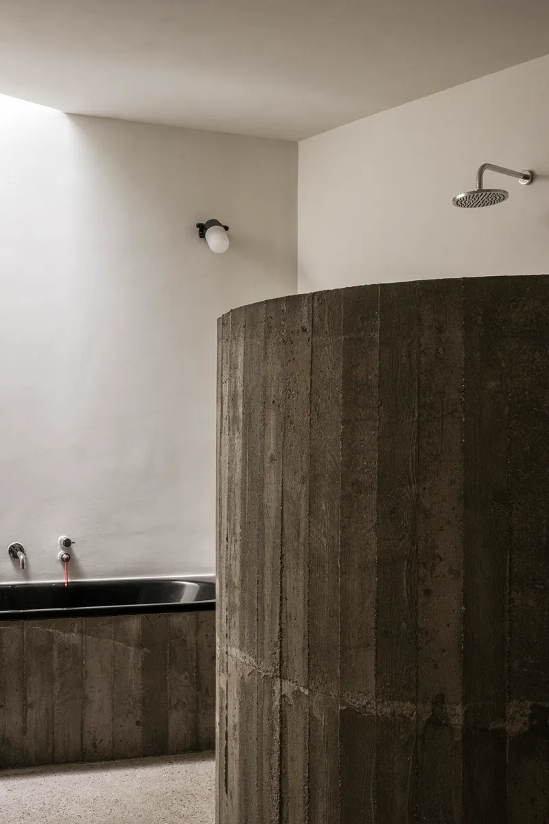 Curved board-formed concrete shower wall with wall-mounted rainfall showerhead and minimal fixtures