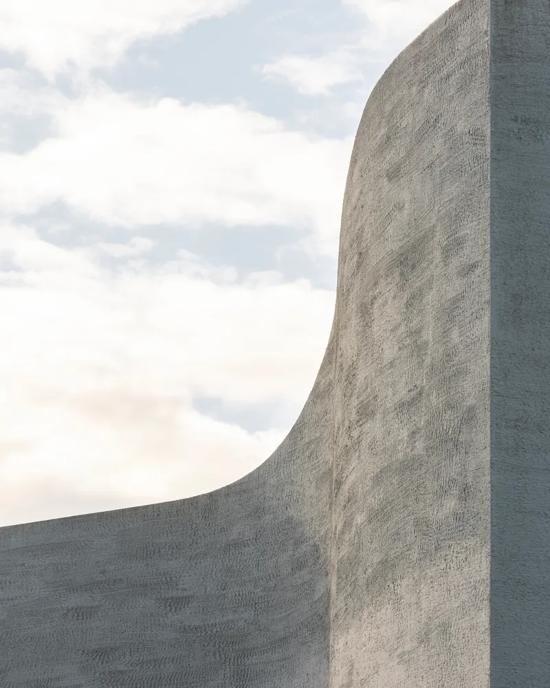 Curved board-formed concrete wall rising against a cloudy sky