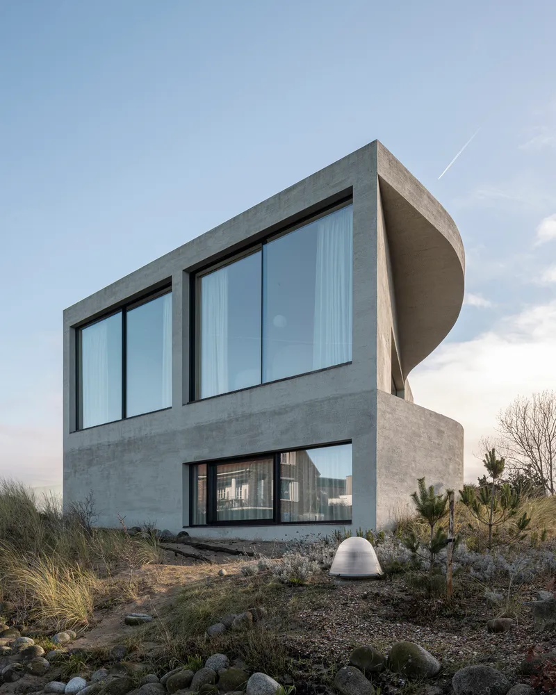 Rear facade at dusk with large glazed openings and cylindrical roof element above planted dunes