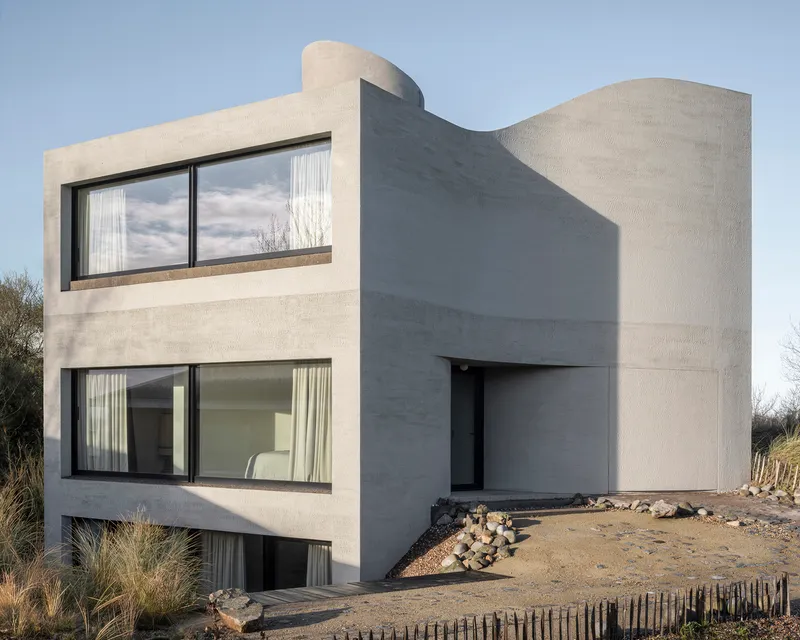 Three-storey concrete facade with horizontal band windows and curved roofline set in dune landscape