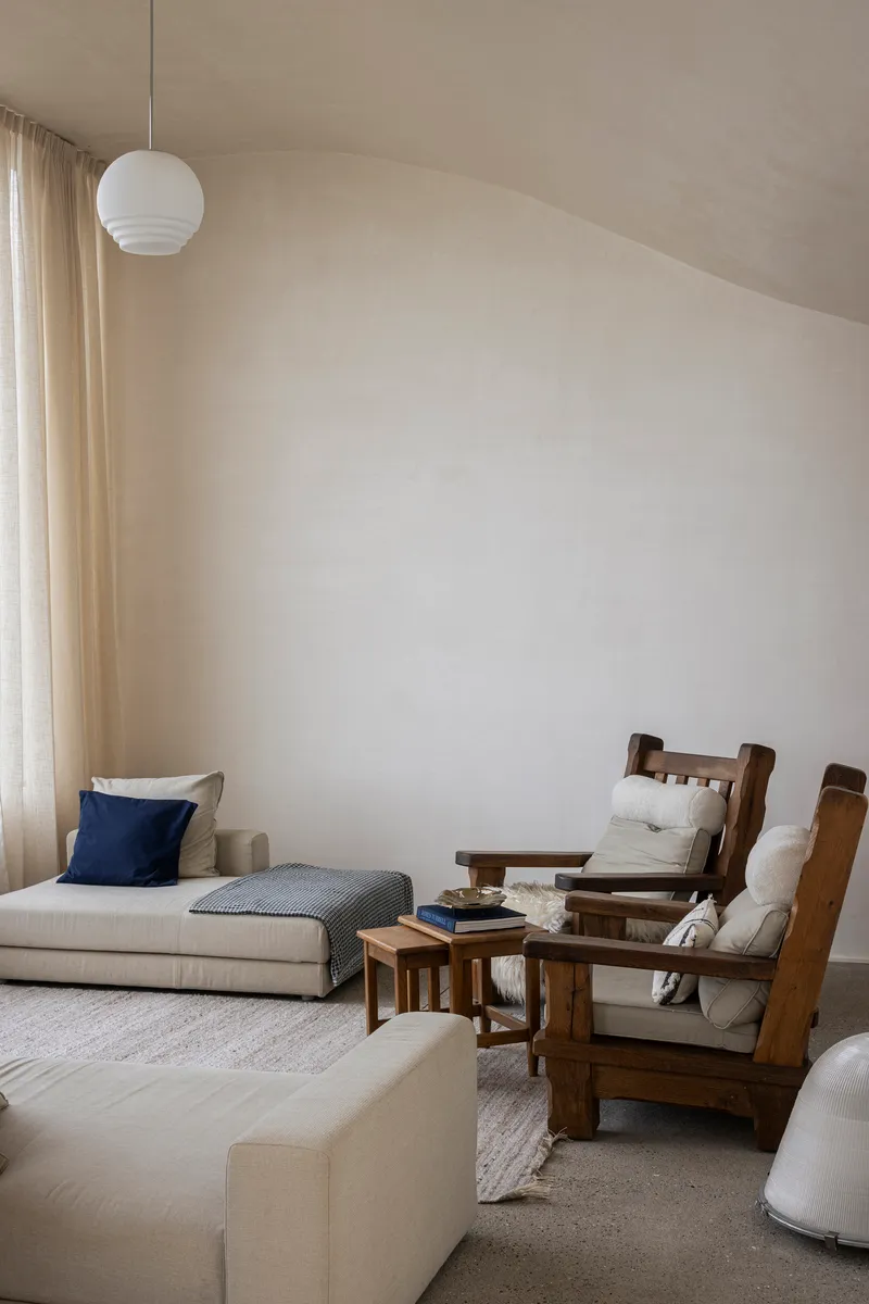 Living room with sloped ceiling, globe pendant light, and timber lounge chairs in soft daylight