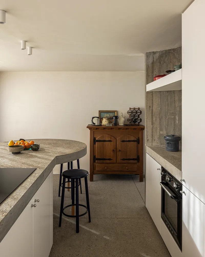 Kitchen with curved concrete island, terrazzo floor, and board-formed concrete wall in natural light