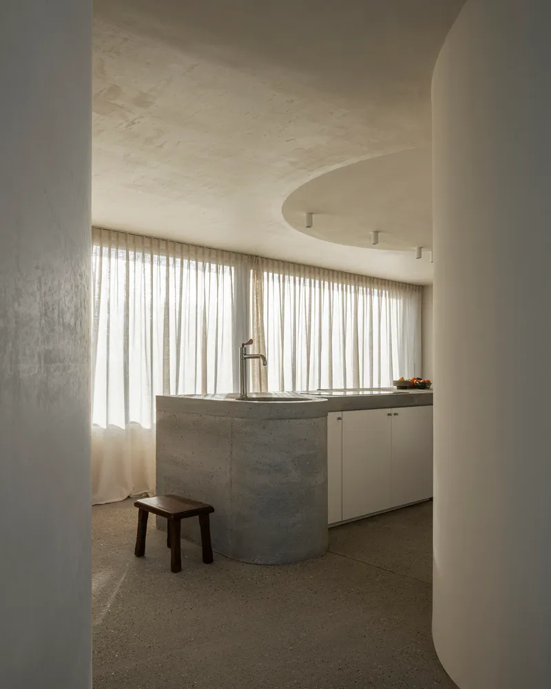 Arched doorway framing kitchen counter with board-formed concrete base and full-height curtained window