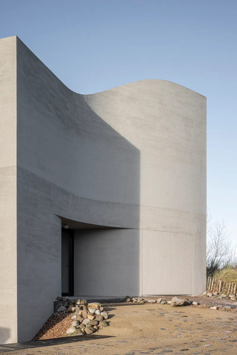 Exterior view of the curved concrete volumes with recessed entrance and cylindrical tower
