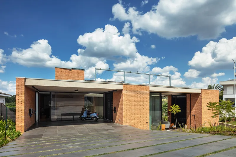 Street facade with orange brick volumes and recessed glazing beneath white clouds in blue sky