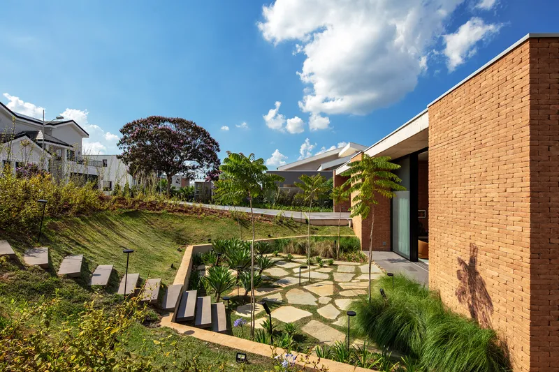 Sloping garden with stone paving and young palms adjacent to orange brick wall under afternoon sun